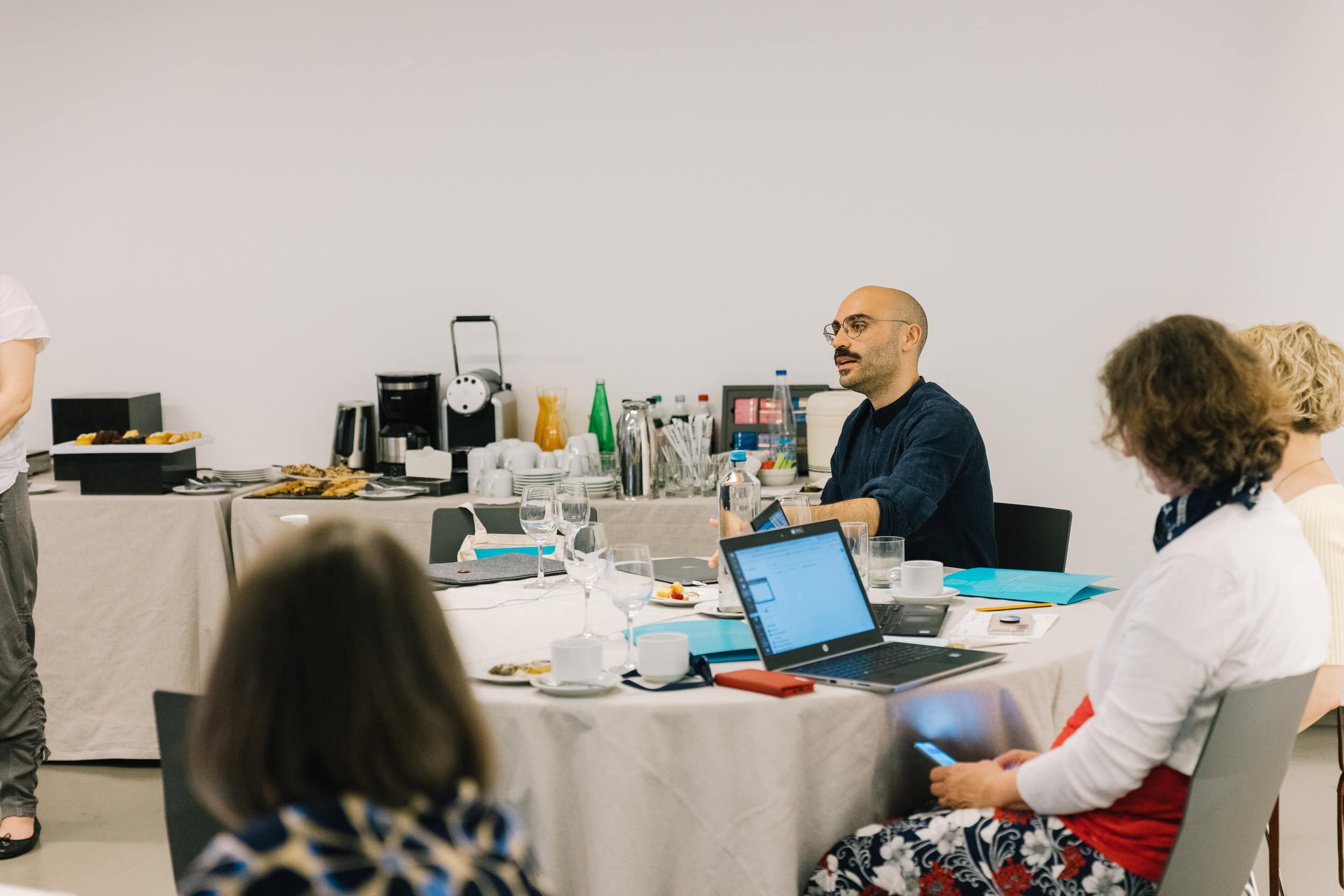A workshop participant works on a laptop while seated at a conference table, with notes and glasses on the table nearby.